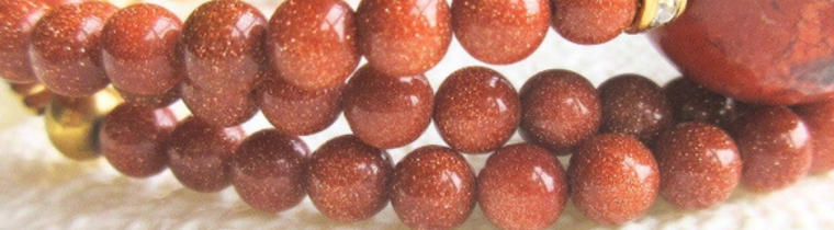 ゴールドストーンビーズの接写。赤茶色の中にきらめく粒が美しく輝く、上品で華やかな天然石ネックレスの一部。