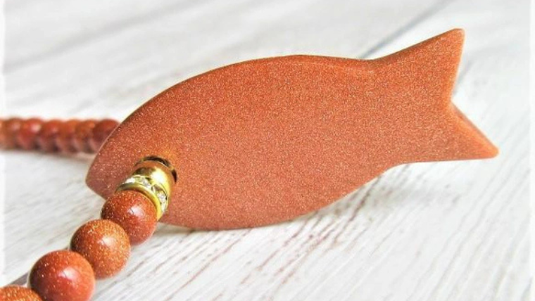 魚のかたちをしたトップが特徴のゴールドストーンネックレス。細かなラメが輝くユニークなデザイン。