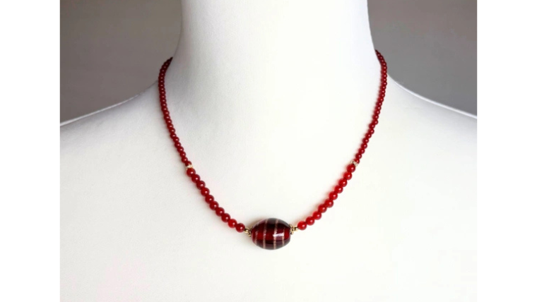 中央のレッド&ブロンズとんぼ玉が印象的な、赤めのうとガーネットのネックレスを身につけた着用イメージ。落ち着いた赤色が首元を華やかに見せる大人向けのアクセサリー。