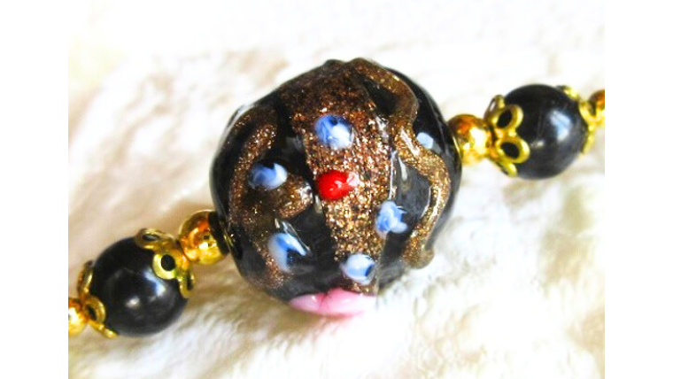 ヴェネチアンとんぼ玉のクローズアップ。黒地に金彩や青・赤の模様が施された一点ものビーズが輝くオニキスネックレスの中心パーツの写真。