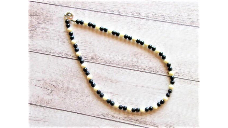 白と黒の天然石ビーズを使用したネックレスを木目の背景に平置きした画像。シンプルで日常使いしやすいデザインがわかる商品写真。